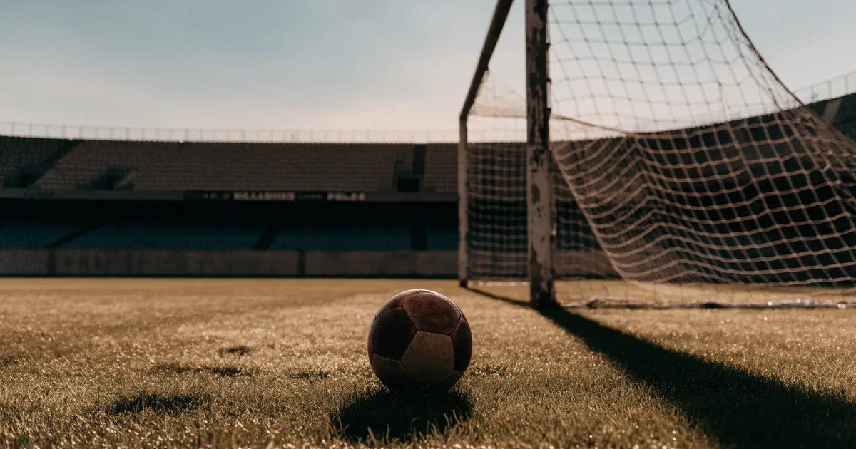 Ein Fußball liegt im Strafraum direkt vor dem Tor mit Netz, im Hintergrund leere Ränge bei Dämmerung.
